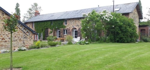 La Longère garden view at Le Petit Lustucru B&B in Avranches, featuring stone buildings with lush green lawn and climbing ivy