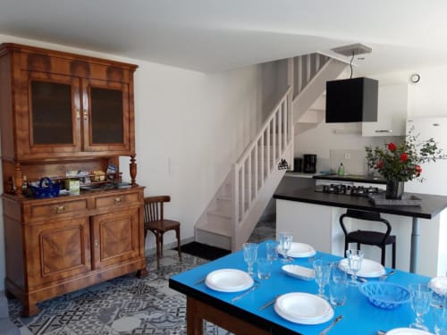 Le Petit Lustucru dining room with blue table, wooden hutch, kitchen, and staircase in Avranches