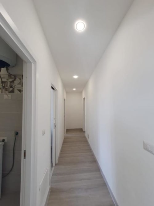 Corridoio luminoso e moderno con illuminazione incassata, pareti bianche e pavimento in legno nell'appartamento Siracusa Sun&Home