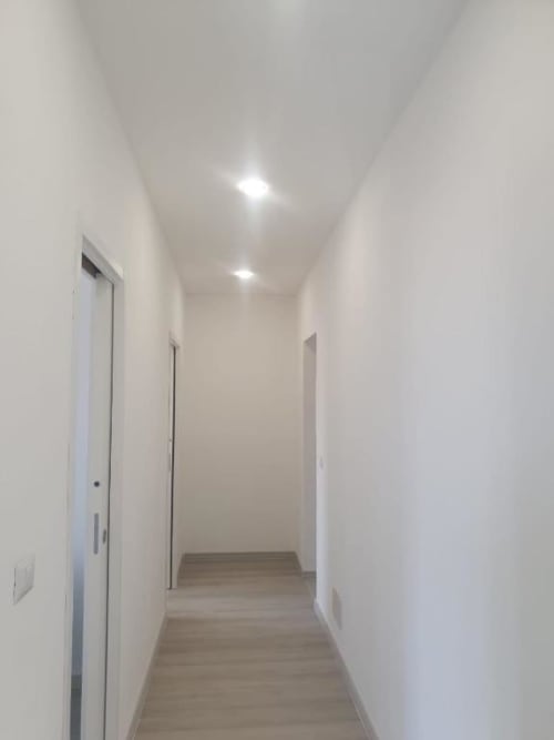 Corridoio moderno con pareti bianche, luci incassate e pavimento in legno nell'appartamento Siracusa Sun&Home