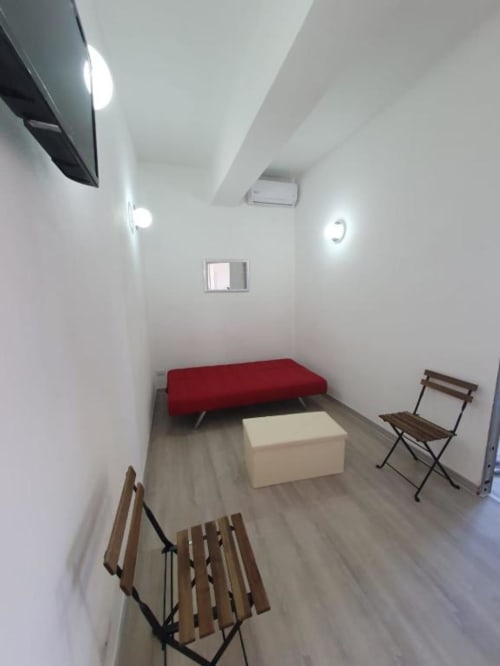 Soggiorno moderno nell'appartamento di Siracusa con divano rosso, tavolo bianco, sedie in legno e illuminazione luminosa