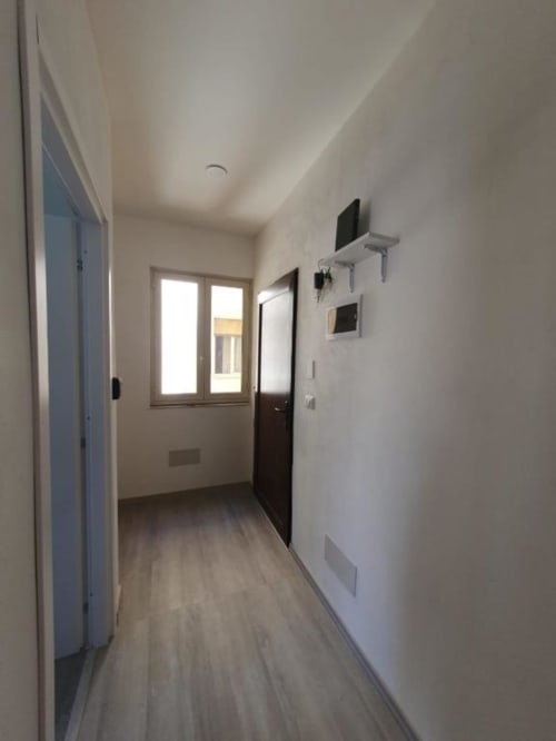 Corridoio moderno dell'appartamento Siracusa Sun&Home con pavimenti in legno, pareti bianche e porta d'ingresso con vista sulla città