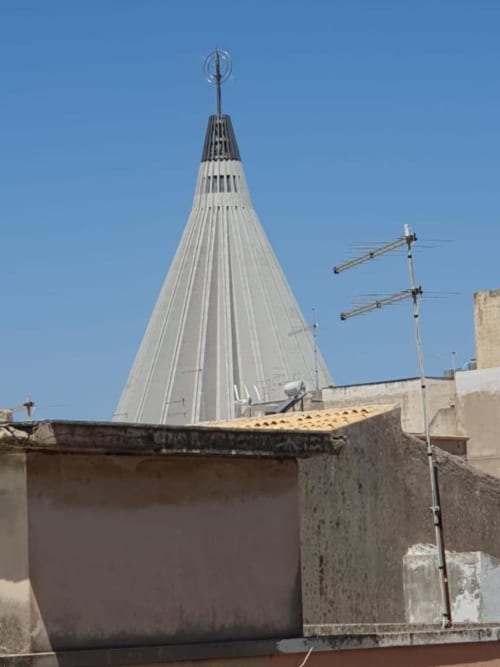 Moderno campanile conico a Siracusa, IT, visibile dal balcone dell'appartamento con cielo blu terso