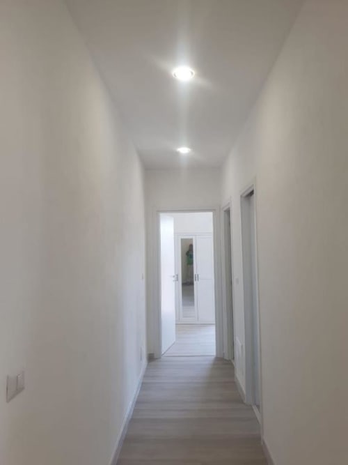 Corridoio moderno dell'appartamento a Siracusa con pareti bianche, illuminazione a incasso e pavimento in legno che conduce alle stanze
