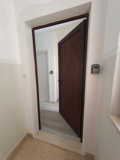 Porta in legno scuro che si apre su un corridoio nell'appartamento monolocale Siracusa Sun&Home con pareti bianche e pavimento in piastrelle