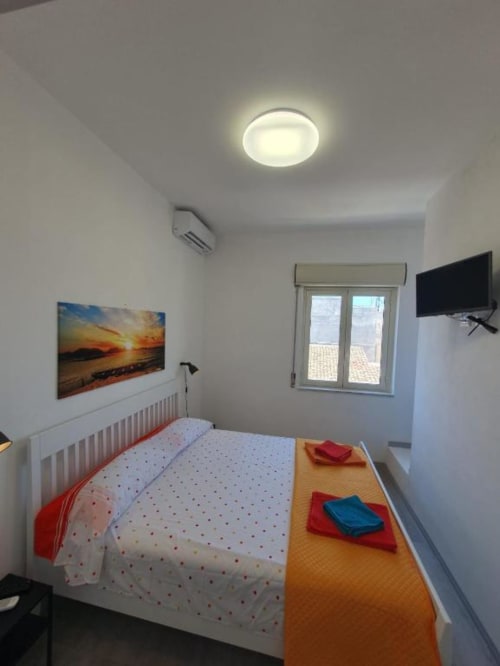 Bright bedroom at Siracusa Sun&Home with white bed, TV, window overlooking city, ceiling light, and modern furnishings