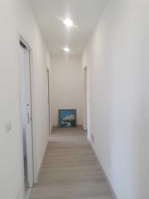 Corridoio moderno nell'appartamento Siracusa Sun&Home con pareti bianche, pavimento in legno e opera d'arte blu