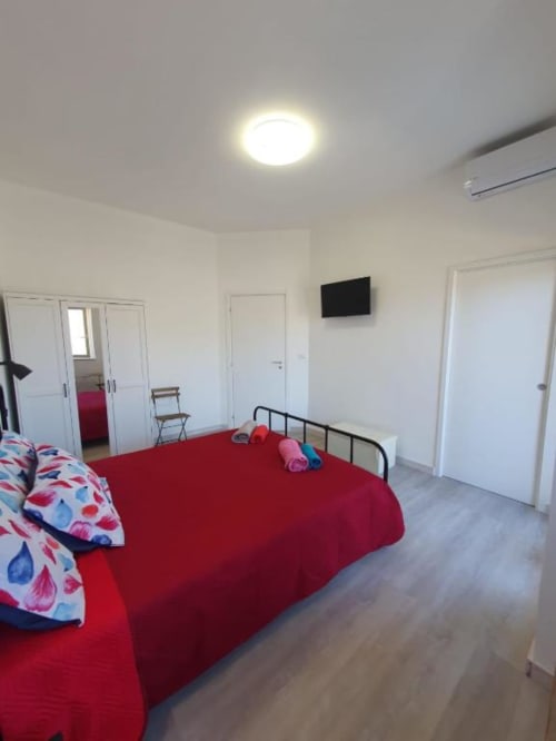Bright bedroom in Siracusa apartment with red bed, white wardrobe, TV, and modern amenities