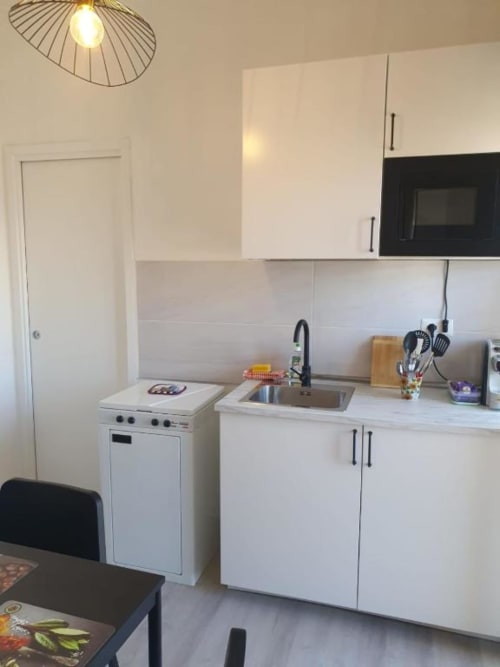 Moderna cucina bianca con fornello, lavandino e microonde nell'appartamento Siracusa Sun&Home