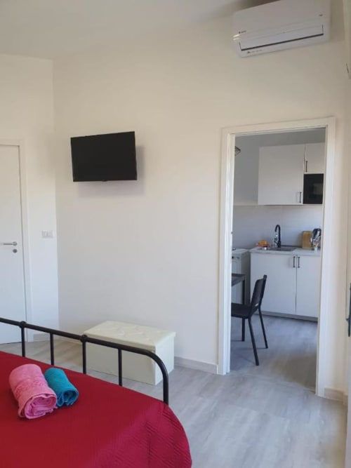 Camera da letto moderna con letto rosso, TV a parete, panca contenitore bianca e accesso alla cucina in appartamento a Siracusa