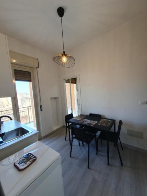 Cucina e zona pranzo moderna con tavolo nero, sedie, lampada a sospensione e balcone con vista città a Siracusa Sun&Home