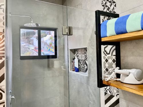 Modern bathroom at Anita Ocean View hotel in Puerto Vallarta featuring glass shower, wall-mounted TV, wooden shelves with