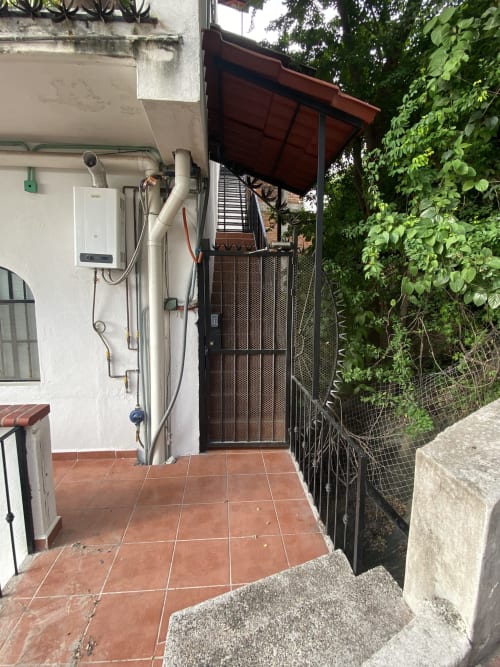 Compact outdoor patio area at Anita Ocean View Puerto Vallarta with white wall, water heater, black metal gate, and lush