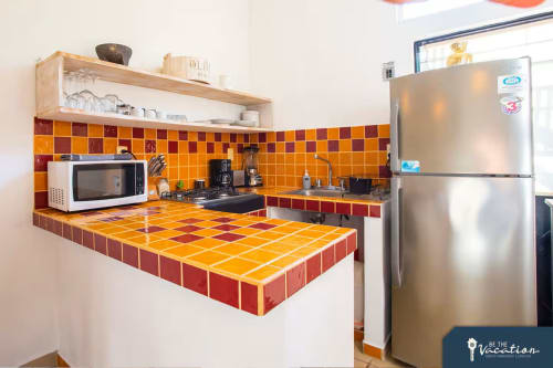 Colorful kitchen with orange and red tiled counters and backsplash, stainless steel refrigerator, and white microwave in