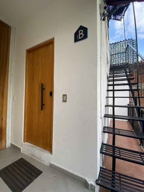 Room B entrance at Anita Ocean View hotel in Puerto Vallarta with wooden door, white walls, and metal staircase leading to