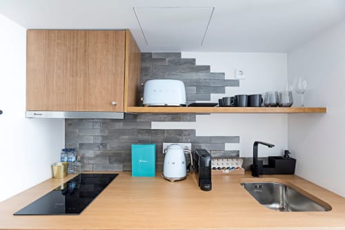 Kitchenete moderna em estúdio de hotel no Porto com bancada em madeira, fogão por indução, pia e eletrodomésticos em aço inoxidável