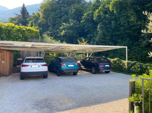 Three parked cars under a modern carport at Verdolivo B&B in Sale Marasino, surrounded by lush green trees and mountains.