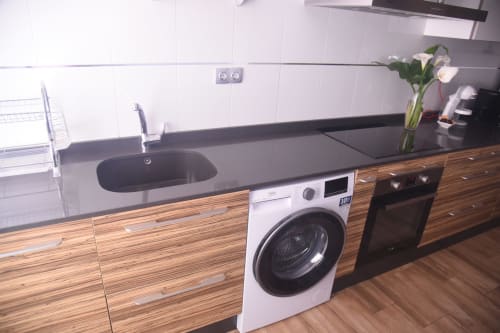 Modern kitchen with dark countertop, white washing machine, black oven, and wooden cabinetry in Benavente city apartment