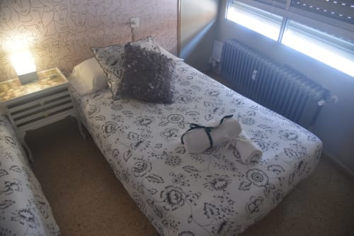 Single bed with floral bedding in Benavente city center apartment, window with radiator visible
