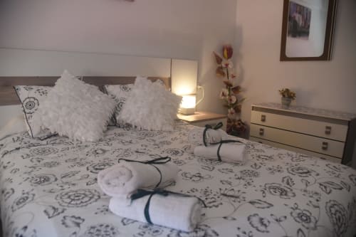 Dormitorio de apartamento turístico en Benavente con almohadas blancas decorativas, ropa de cama estampada, lámpara de noche y toallas enrolladas