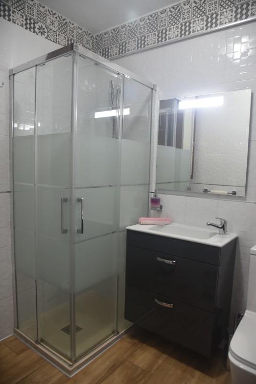 Modern bathroom in Benavente tourist apartment with shower enclosure, black vanity, and decorative tile border