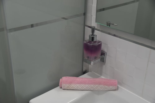Modern bathroom sink with pink and white towel, purple soap dispenser, and mirror in Benavente hotel apartment
