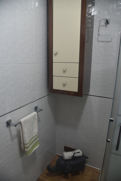 Modern bathroom with white tile walls, cream-colored vanity cabinet with drawers, towel rack, and glass shower enclosure in