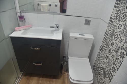 Modern bathroom in Benavente apartment with black vanity, white sink, patterned tile shower, and toilet