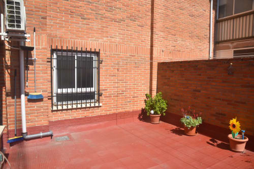 Sunny terrace with red tile floor, potted plants, and black barred window at Benavente tourist apartment