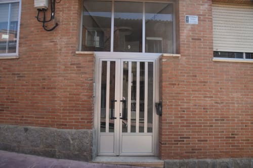 Entrada del apartamento turístico de Benavente con puertas de cristal blanco y fachada de ladrillo rojo en el centro de la ciudad