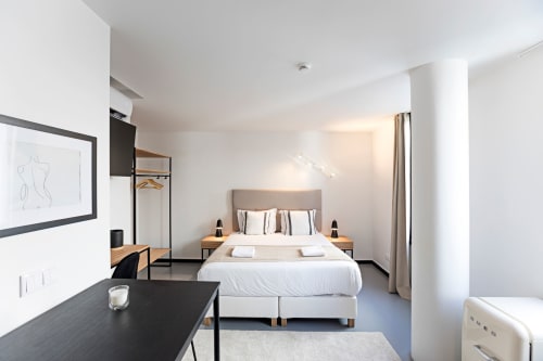 Modern hotel studio in Porto with queen bed, white bedding, wooden nightstands, desk area, kitchenette, and city views