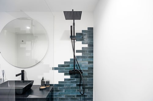 Baño moderno del hotel Benefit Collection Porto con lavabo negro, espejo redondo, ducha de efecto lluvia y acento de ladrillo turquesa