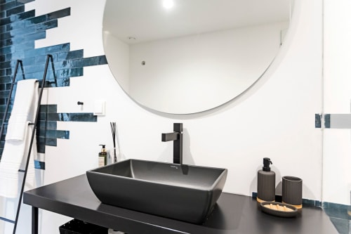 Cuarto de baño moderno del hotel Benefit Collection Porto con lavabo negro, espejo redondo y acentos de azulejos azules