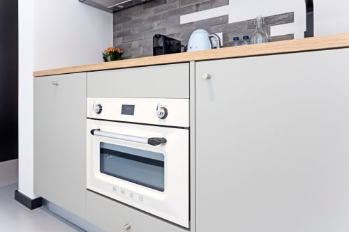 Pequeña cocina blanca y moderna en estudio de hotel en Oporto con horno SMEG, placa de cocción y encimera de madera