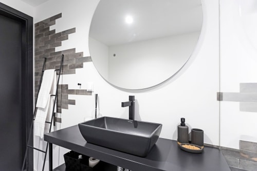 Baño moderno con lavabo rectangular negro, espejo circular y azulejos oscuros en la suite Collection Benefit Porto