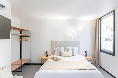 Modern studio bedroom in Porto hotel with double bed, wooden nightstands, flat-screen TV, city view window, and minimalist