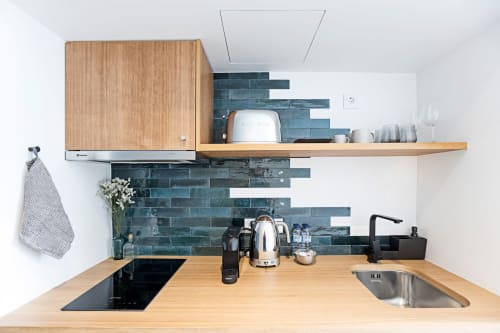 Modern kitchenette in Porto hotel studio with wooden counters, blue tile backsplash, stove, sink, and coffee machine