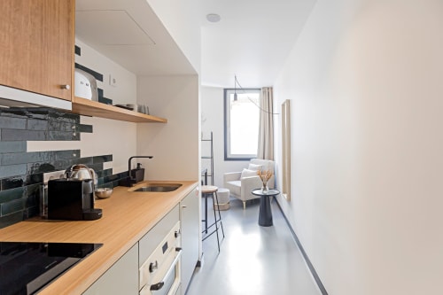 Modern hotel kitchenette in Porto with wooden countertop, dark tile backsplash, and seating area with window view