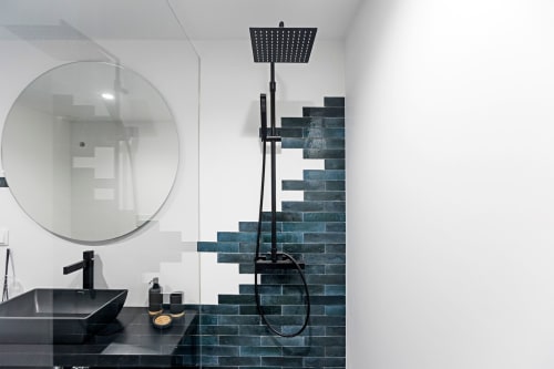 Modern bathroom in Porto hotel with black sink, round mirror, rainfall showerhead, and teal subway tile accent wall