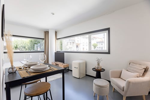 Moderno estudio en Oporto con mesa de comedor negra, zona de estar beige, refrigerador crema y vistas a la ciudad