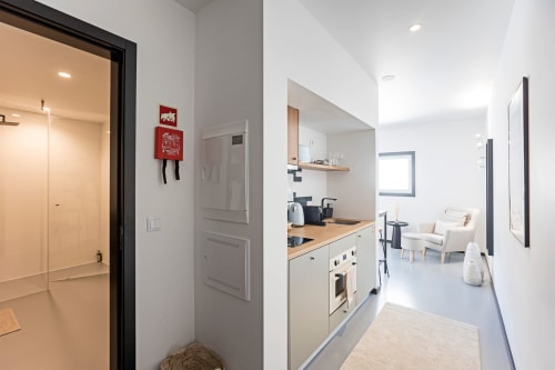 Pequeña cocina de estudio moderno con encimeras de madera, gabinetes blancos y sala de estar en hotel de Porto