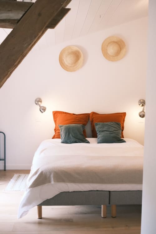 Chambre moderne à la Maison Monsieur Léger avec coussins orange et bleu canard, literie blanche et détails de plafond en bois à Montaut
