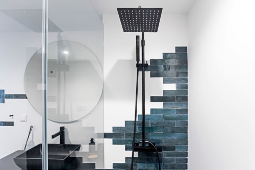 Baño moderno en estudio de hotel en Oporto con espejo redondo, accesorios negros, pared de acento con ladrillos color azul verdoso y alcachofa de ducha de efecto lluvia
