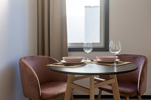 Studio de l'hôtel Porto moderne avec table ronde noire, deux chaises bordeaux, couverts et verres à vin