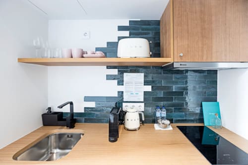 Kitchenette moderne dans chambre hôtel Porto avec comptoirs bois, carrelage subway turquoise, cuisinière, évier et cafetière