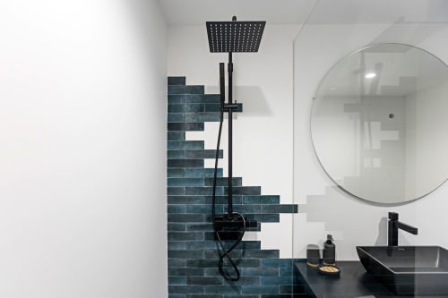 Salle de bains moderne dans un hôtel de Porto avec carrelage turquoise, douchette pluie noire, miroir rond et lavabo noir
