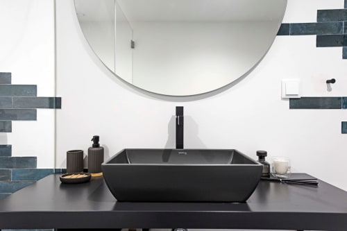 Salle de bains élégante de l'hôtel Porto avec lavabo noir rectangulaire, robinet design, miroir rond et mur d'accent en carrelage foncé