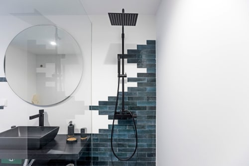 Baño moderno del hotel de Porto con lavamanos negro, espejo redondo y pared de ducha de azulejo verde azulado con alcachofa de lluvia