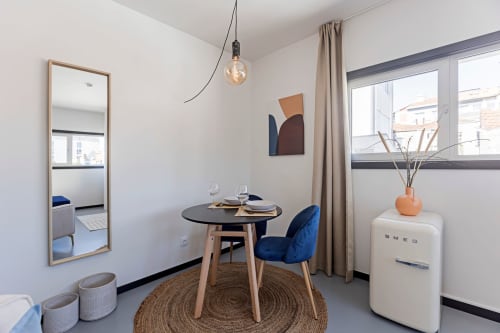 Modern studio apartment in Porto with dining area, blue chair, round table, retro refrigerator, and garden view
