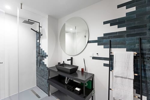 Modern bathroom in Porto hotel with black tile accent wall, round mirror, black sink vanity, and walk-in shower with rainfall